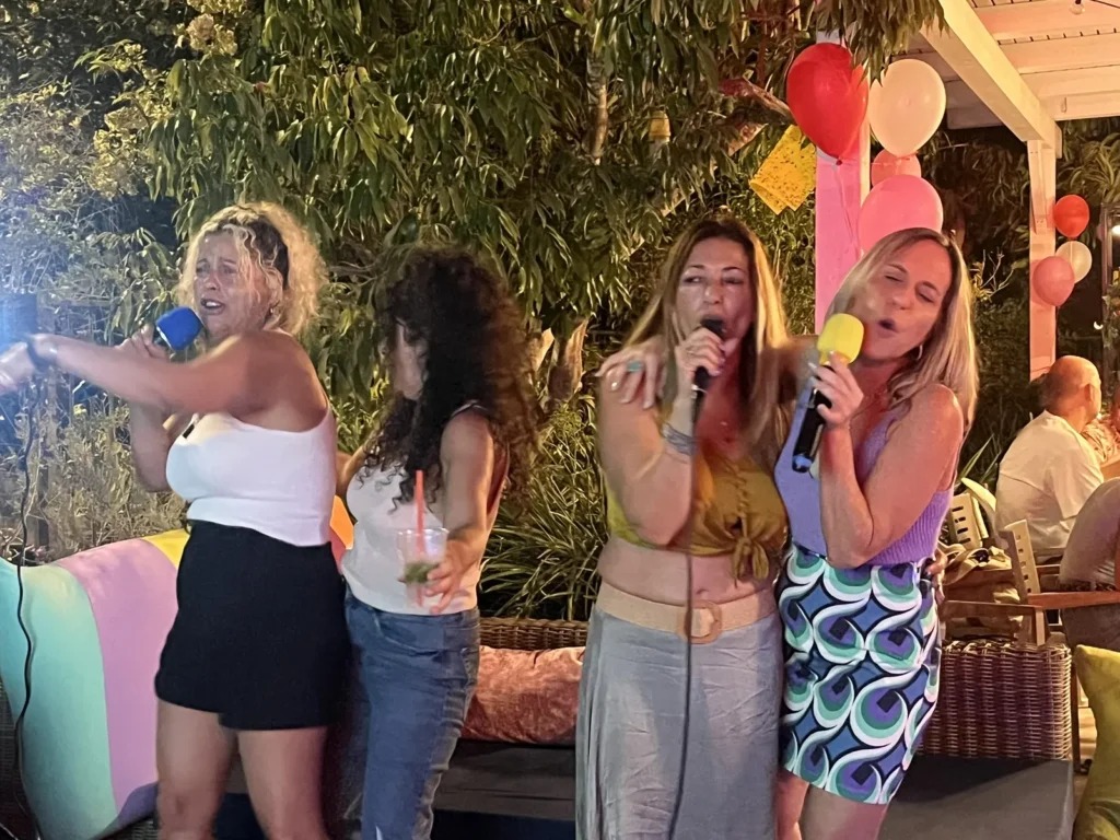 ארבע חברות שרות במיקרופונים צבעוניים במסיבת יום הולדת בחצר