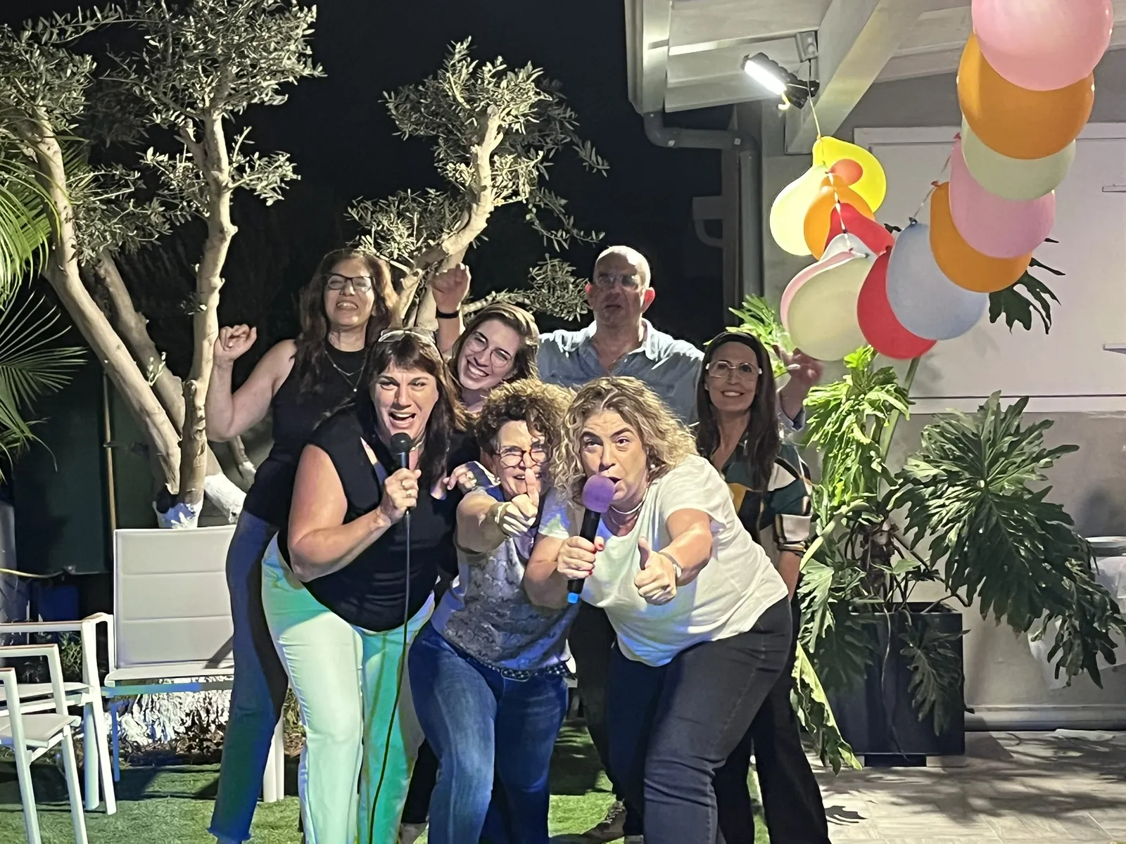 חבורת חברים שרה ומצביעה למצלמה במסיבה בחצר